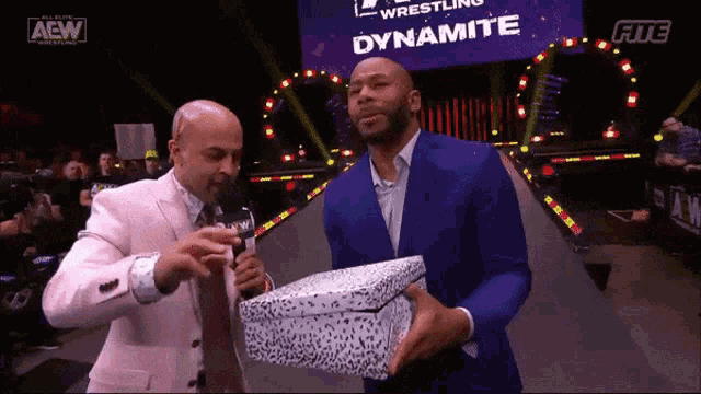 a man in a blue suit is holding a box with dynamite written on it