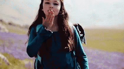 a young girl is blowing a kiss while standing in a field of purple flowers .