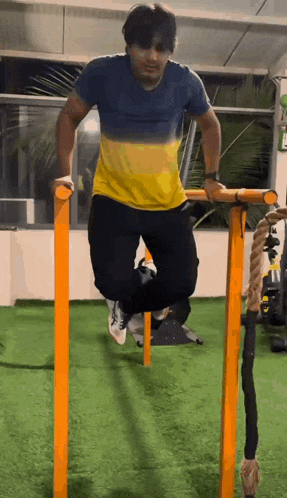 a man in a blue and yellow shirt is doing push ups on a bar in a gym .