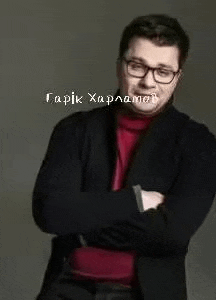 a man with glasses and a red turtleneck is standing with his arms crossed .