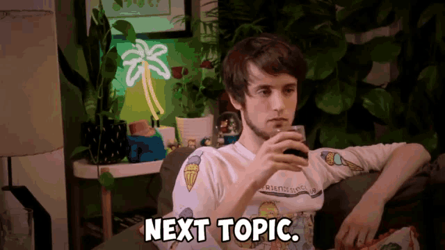 a man sits on a couch with a glass of beer and next topic written on the screen
