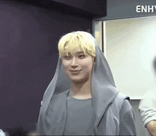 a young man with blonde hair is wearing a gray hoodie and a gray scarf around his head .