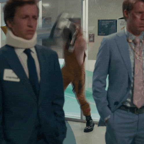 a man wearing a neck brace stands next to another man in a blue suit