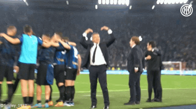 a man in a suit stands on a soccer field surrounded by players