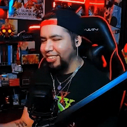 a man wearing a hat and a necklace is sitting in a gaming chair .