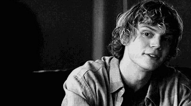 a black and white photo of a young man with curly hair wearing a plaid shirt .