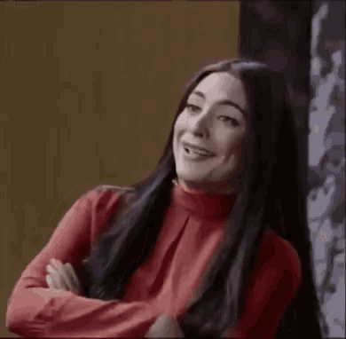 a woman with long black hair is wearing a red turtleneck sweater and smiling .