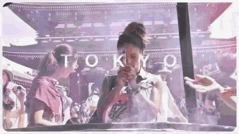 a woman is praying in front of a building with the word tokyo on it