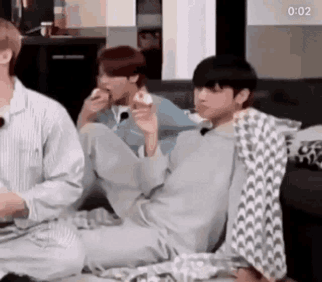 a group of people are sitting on a couch eating food and talking to each other .