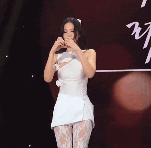 a woman in a white dress making a heart shape