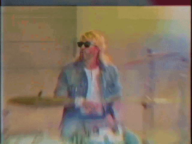 a man wearing sunglasses is playing a drum set in a room .