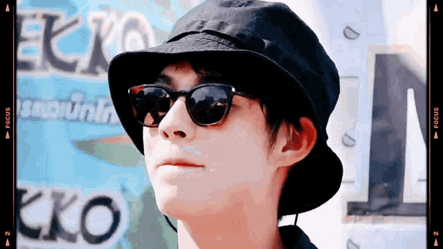 a man wearing a black hat and sunglasses looks at the camera