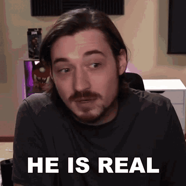 a man with a beard says he is real in front of a desk