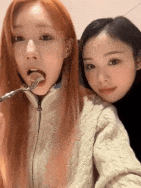 two young women are eating food together with a fork in their mouths .