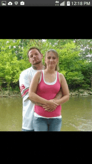 a man and woman are posing for a picture in front of a body of water