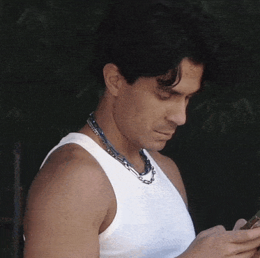 a man wearing a white tank top is looking at his cell phone