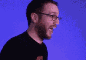 a man with glasses and a beard is laughing against a blue background .