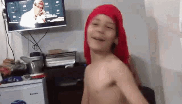a shirtless boy wearing a red head scarf is dancing in front of a television