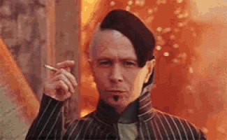 a man with a mohawk and beret is smoking a cigarette in front of a fire .