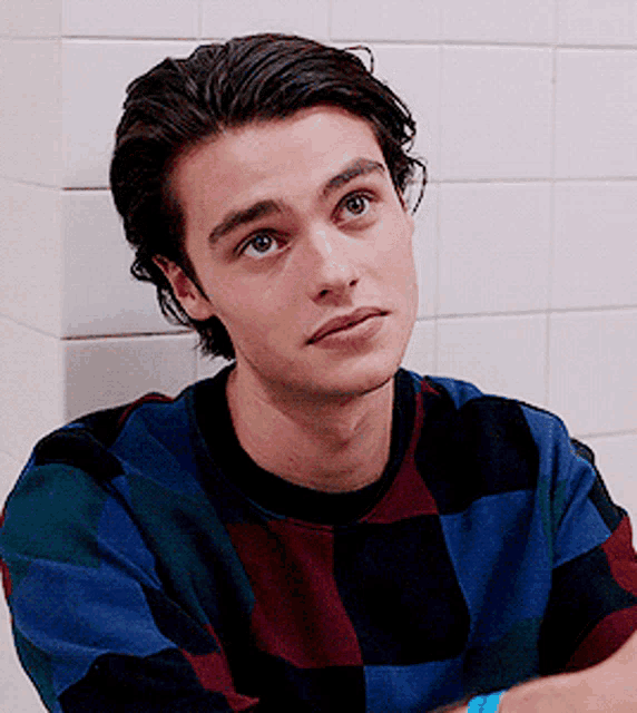 a young man leaning against a wall with his arms crossed