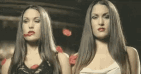 two women with long hair are standing next to each other in a dark room .