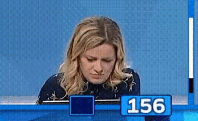 a woman is sitting at a table with a blue sign that says 156 on it .