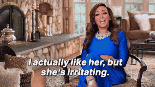 a woman in a blue dress is sitting in a chair and says i actually like her but she 's irritating