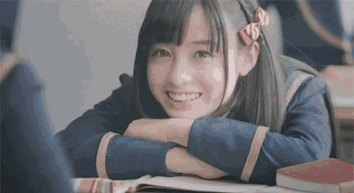 a young girl is sitting at a desk with her head resting on her arms .