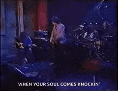 a man is playing a guitar in front of an amplifier while another man stands behind him .