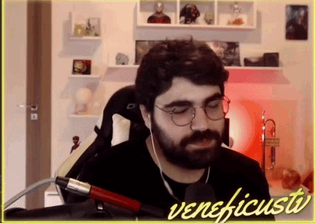 a man with glasses and a beard is sitting in front of a microphone with the name veneficusta written on the bottom