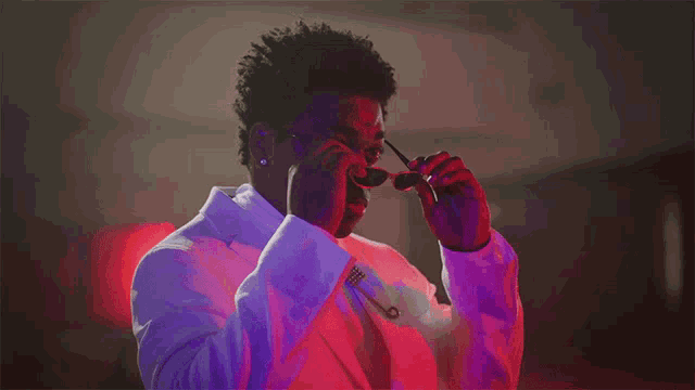 a man in a white suit is adjusting his sunglasses in a red and purple light .
