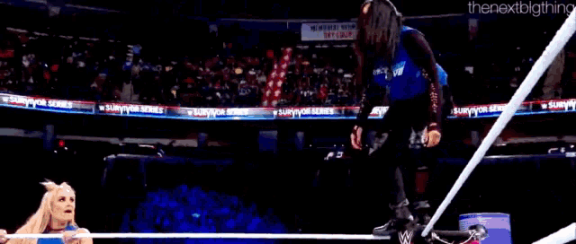 a man in a blue shirt is jumping over a rope in a boxing ring .