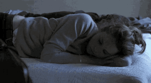 a woman in a sweater is laying on a bed with her eyes closed
