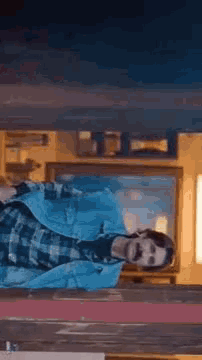 a man in a plaid shirt and a denim jacket is standing in front of a window .