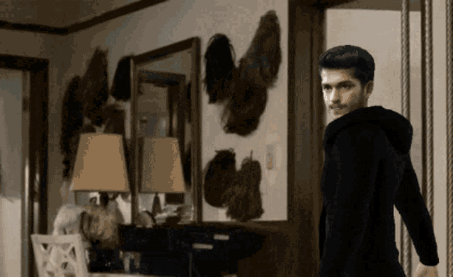 a man in a black hoodie is standing in a room with a lot of wigs on the wall
