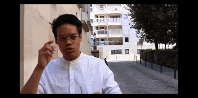 a young man wearing glasses and a white shirt is standing in front of a building