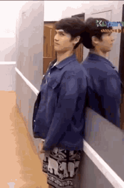 a man in a denim jacket is leaning against a wall .