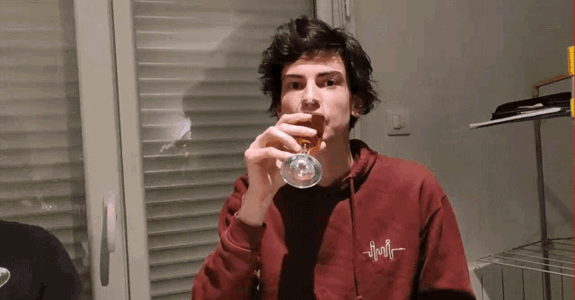 a man in a red hoodie is drinking from a glass with the word apollo on it
