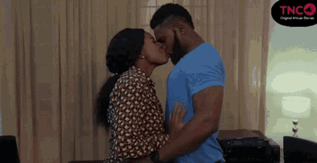 a man and a woman are kissing in a living room with a tnc logo in the corner .