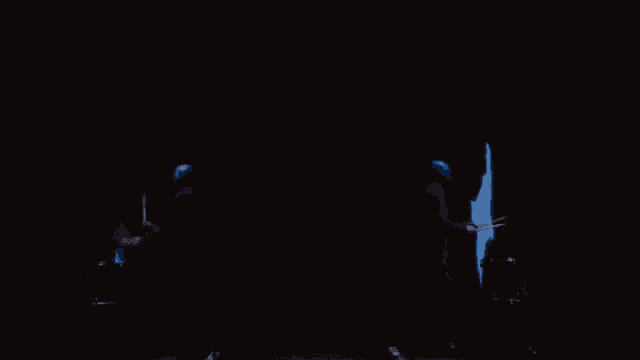 a man in a black suit is playing drums in a dark room