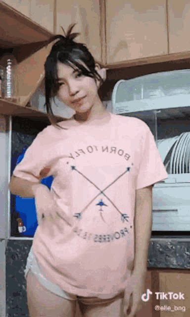 a woman wearing a pink t-shirt is dancing in a kitchen .