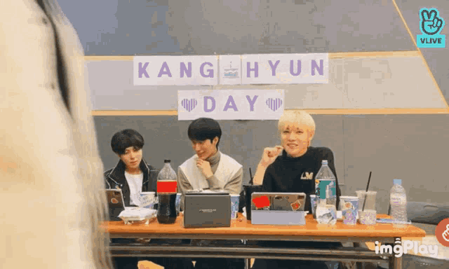 three boys sit at a table with a sign that says kang hyun day
