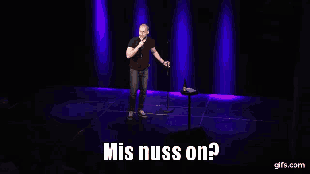 a man stands on a stage with a microphone and says mis nuss on ?