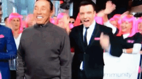 a man in a suit and tie stands next to another man in a sweater