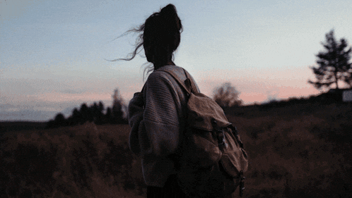 a woman with a backpack stands in a field