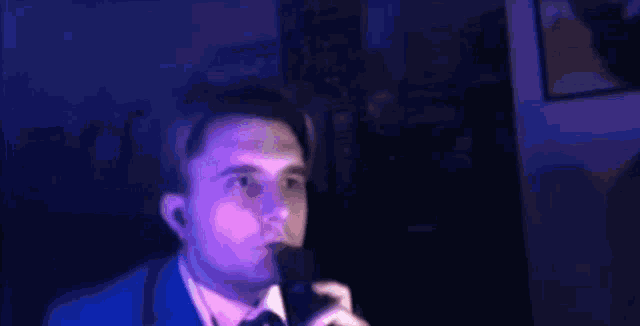 a man in a suit and tie is smiling in a dark room with blue lights .