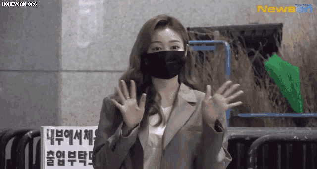 a woman wearing a mask and a suit is standing in front of a sign that says newsan