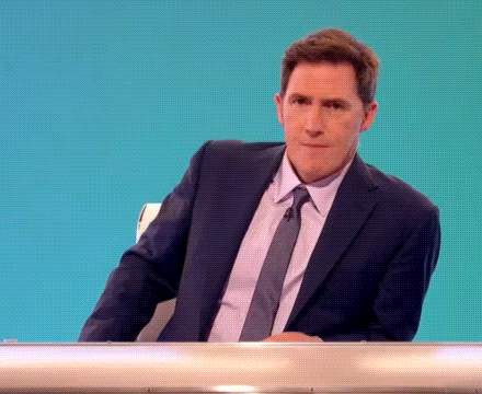 a man in a suit and tie is sitting at a table with his hands folded .