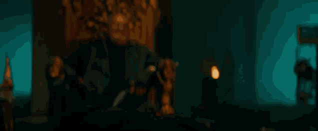 a man with a beard is sitting on a throne in a dark room and pointing at something