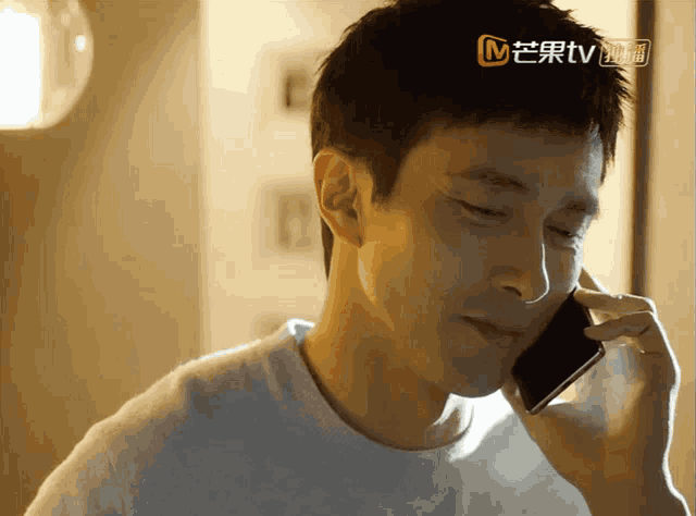 a man is talking on a cell phone with a chinese tv advertisement behind him
